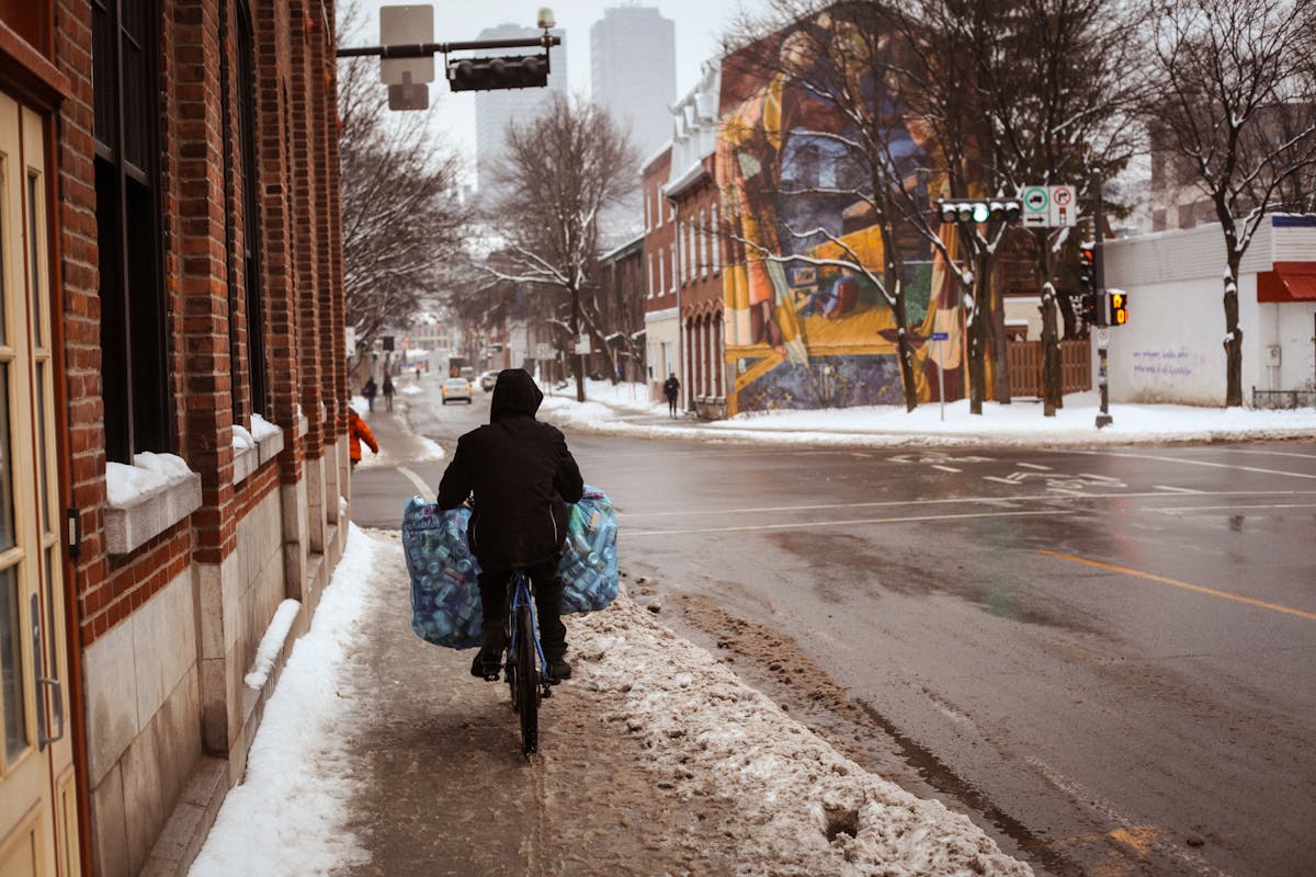 Person on Bike with Bags with Cans on Sidewalk in City in Winter