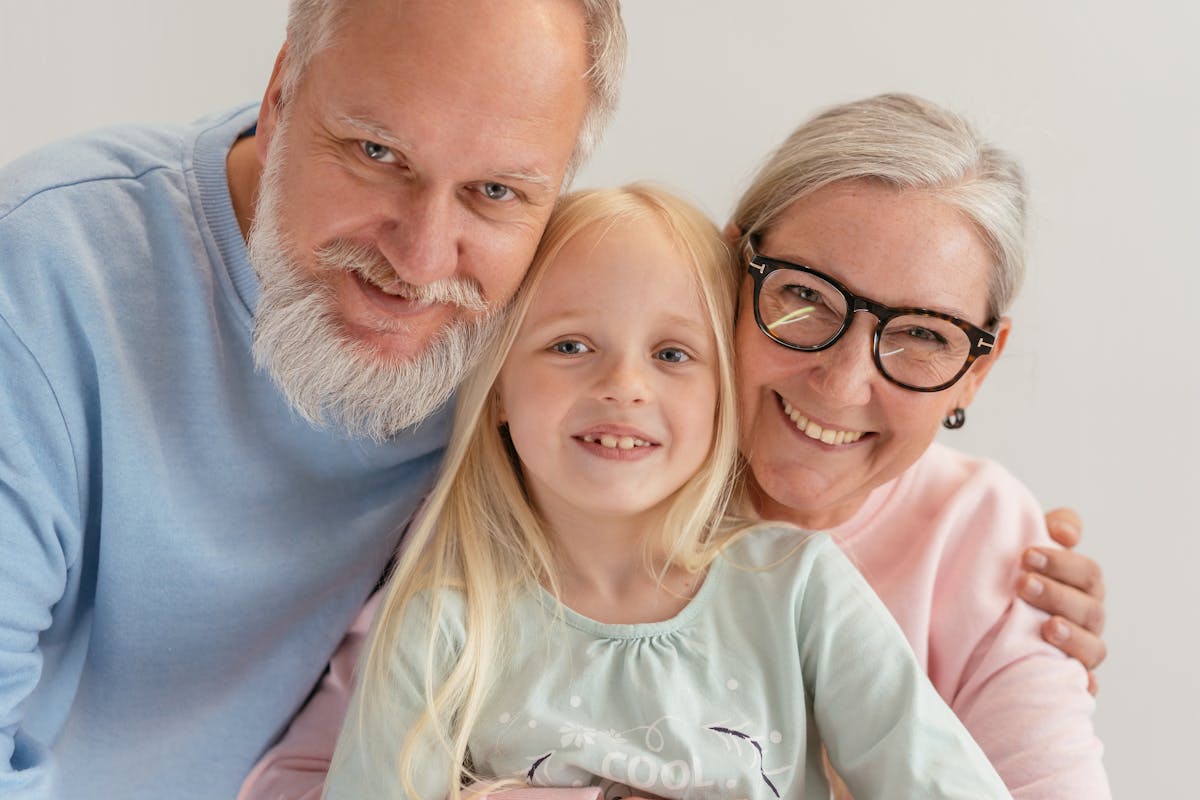 Close-Up Shot of a Happy Elderly Couple with Their Grandchild Hugging while Looking at Camera